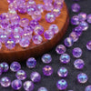 A collection of small, round purple amethyst crystal glass beads scattered on a dark surface next to a wooden board.