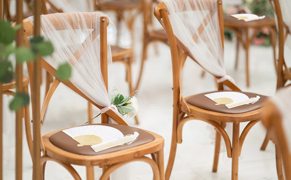 Elegant paper hand fans with gift bags and thank you cards displayed on wooden chairs.