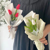 A bouquet of artificial tulips, featuring red and white flowers, wrapped in light green paper.