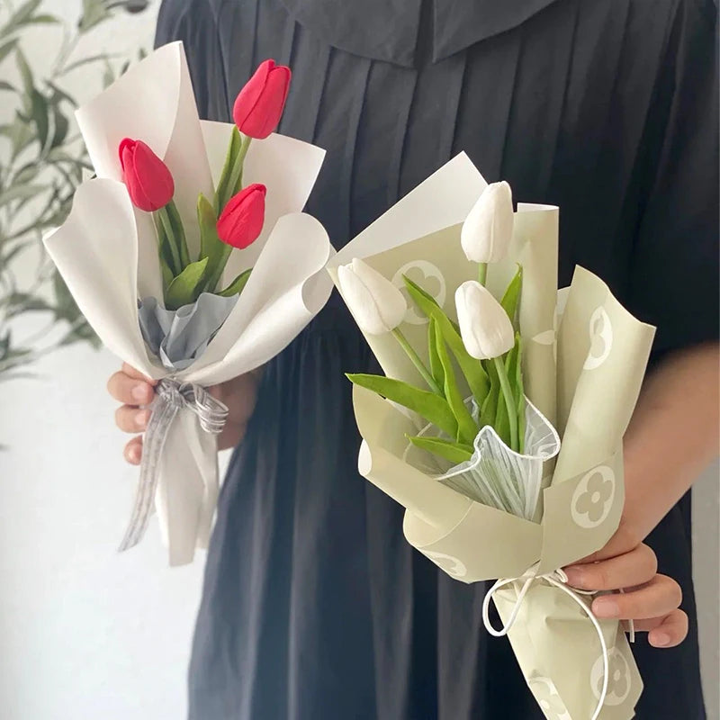 A bouquet of artificial tulips, featuring red and white flowers, wrapped in light green paper.