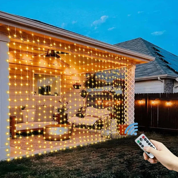 Warm yellow fairy lights illuminate a modern house facade and patio area at dusk.