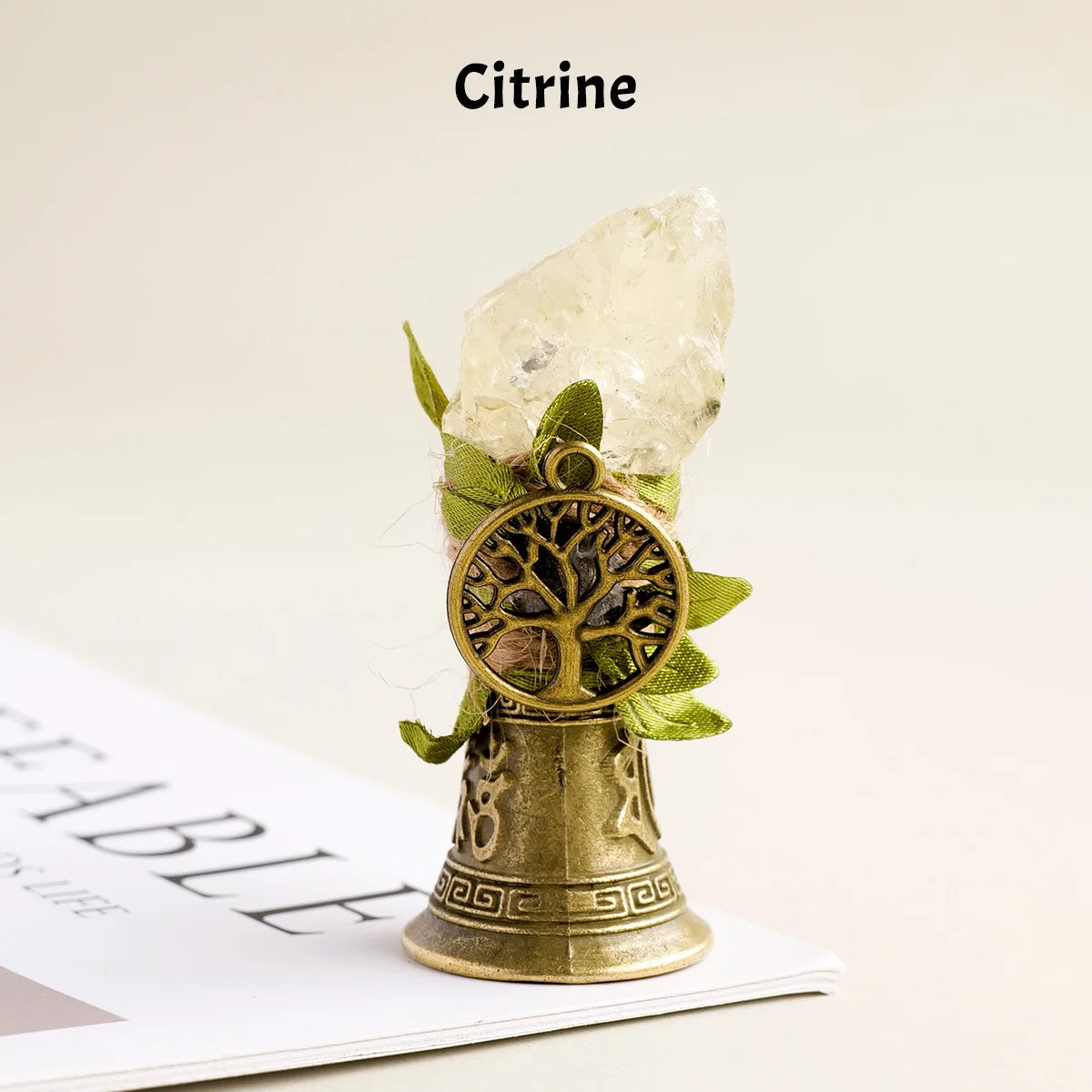 A natural citrine crystal is displayed atop a brass bell with a copper finish.