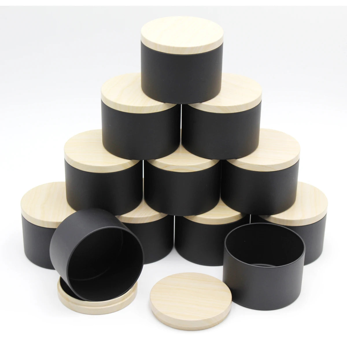 A set of black and natural wood metal candle tins with lids arranged in a pyramid formation.