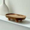 A light brown elliptical wooden storage tray with small feet resting on a white shelf.