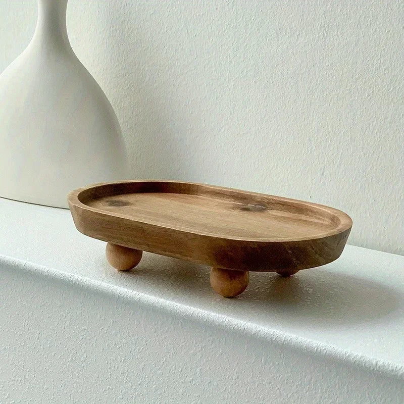 A light brown elliptical wooden storage tray with small feet resting on a white shelf.