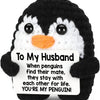 A black and white crochet penguin plush doll with a sign that reads To My Husband You're My Penguin