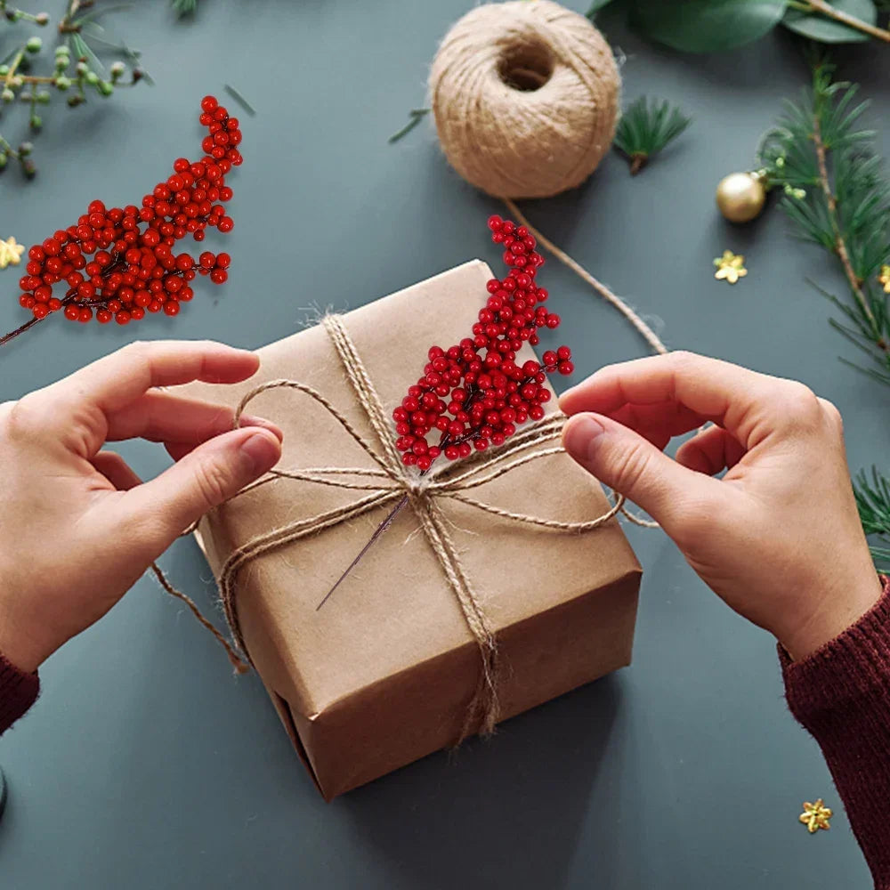 Hands tie a brown gift box with red artificial holly berry stems for Christmas decor