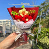 A hand holds a bouquet of handmade crochet flowers featuring red and yellow blooms wrapped in clear cellophane.