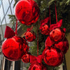 A cluster of glossy red round foil balloons tied to a green Christmas tree branch.