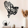 Black silhouette of open praying hands with a cross pendant on a white wall.