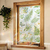 A window framed in wood displays a decorative privacy film featuring green foliage and floral accents.
