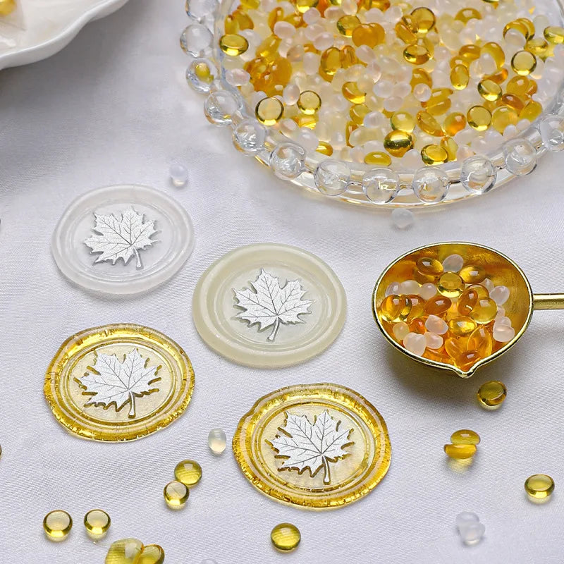 A collection of transparent wax sealing beads in yellow and amber tones, including a glass bowl and circular molds.