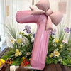 Pink 32-inch number balloons with matte bow decor set of two displayed among greenery and flowers
