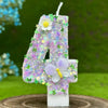 A large purple glitter number four candle decorated with a white flower and a translucent purple butterfly