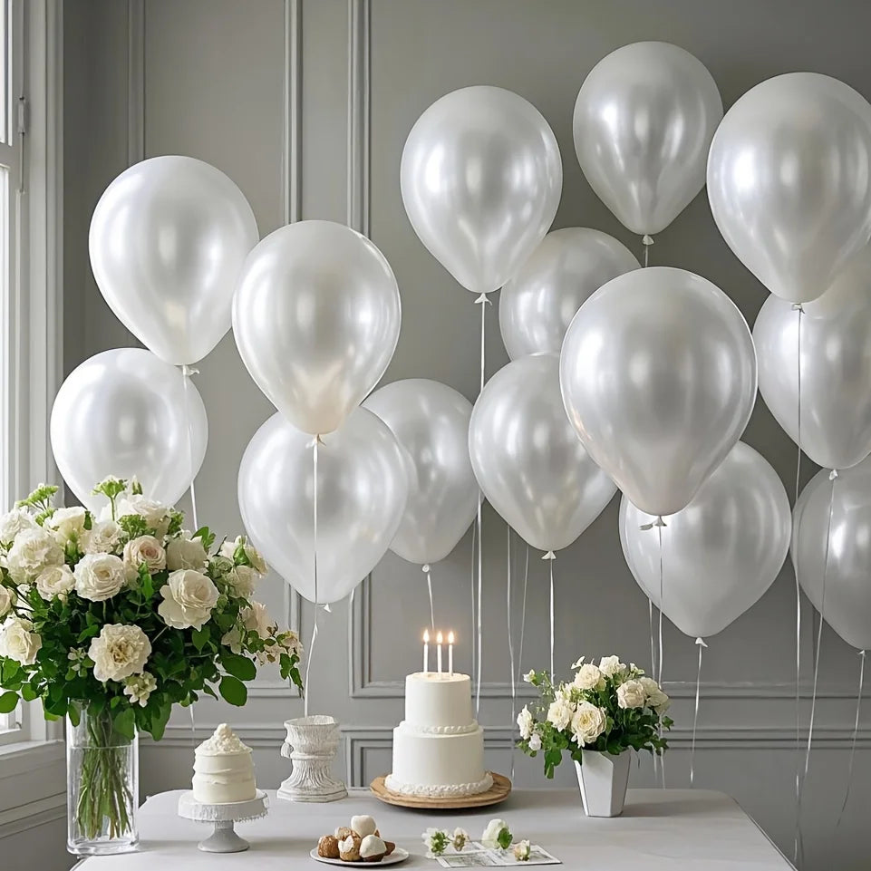A display of pearl white latex balloons, roses, and a tiered cake on a white table for a wedding or party.