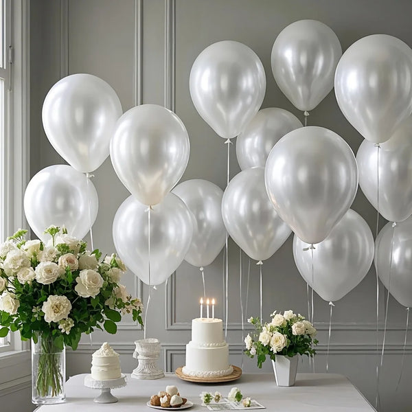A display of pearl white latex balloons, roses, and a tiered cake on a white table for a wedding or party.