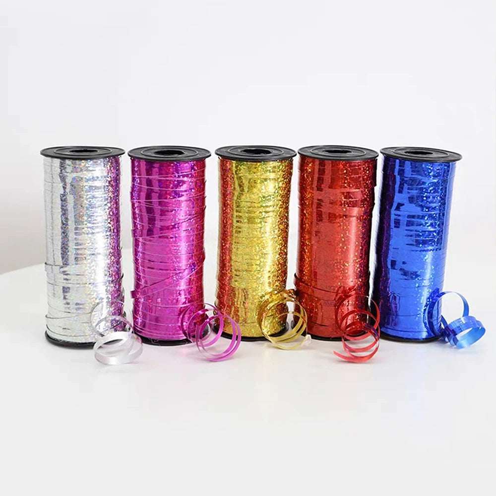 A row of seven rolls of glitter curling ribbon in various colors including silver, pink, gold, orange, red, and blue.