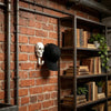 Two decorative skull wall hooks mounted on a brick wall next to a wooden bookshelf.