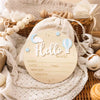 A round light wood birth announcement sign with the word Hello world and blank lines for name date time weight and length is 