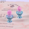Two small, translucent blue resin potion bottles with pink caps displayed on a pink background.