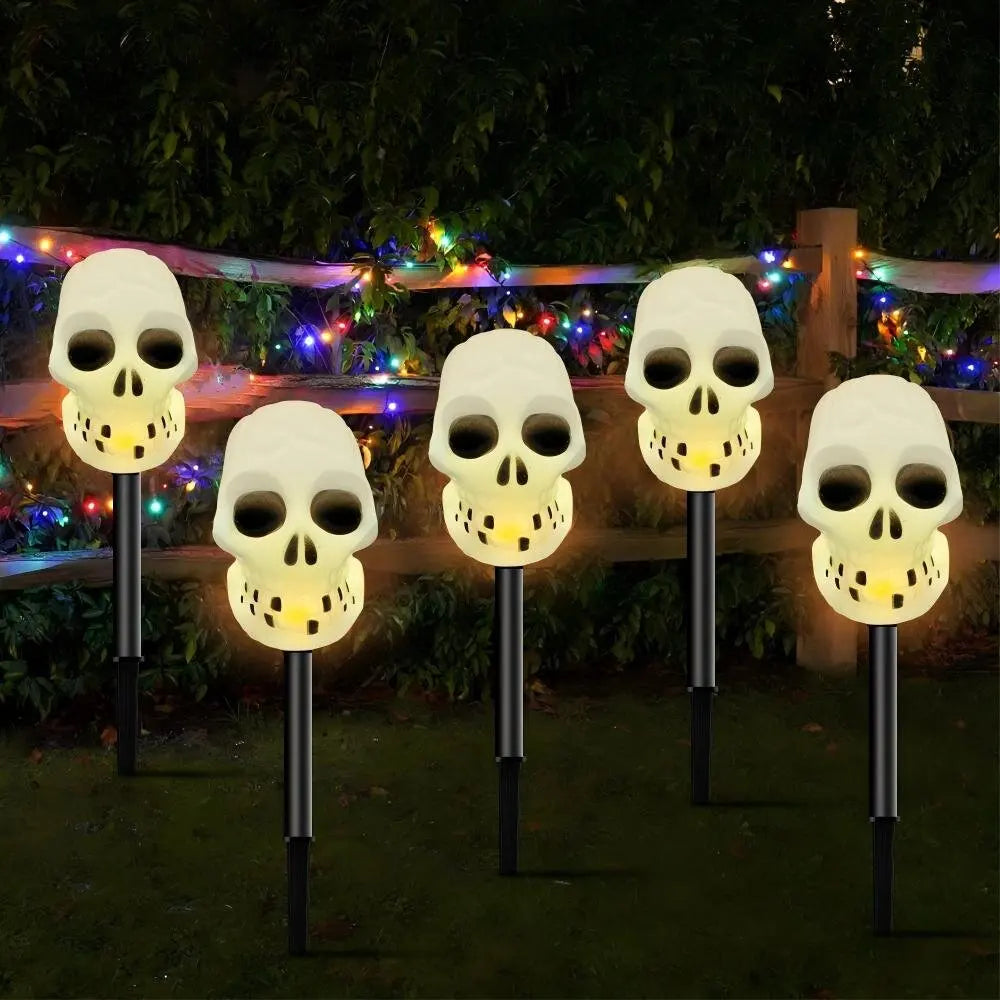 A row of white skull solar pathway lights illuminating a garden area.