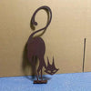 A dark brown wrought iron cat ornament with a curved tail and pointed ears mounted on a blue surface.