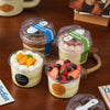 A collection of clear disposable pudding cups with lids and spoons, some filled with layered desserts like mousse and custard