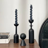 A set of two black, twisted candle holders with dark wax candles displayed on a wooden surface.