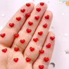 A hand displays numerous small red heart-shaped rhinestones for nail art and crafts.