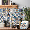 A close-up of self-adhesive tile wall stickers featuring blue, orange, and white geometric patterns on a wooden surface.