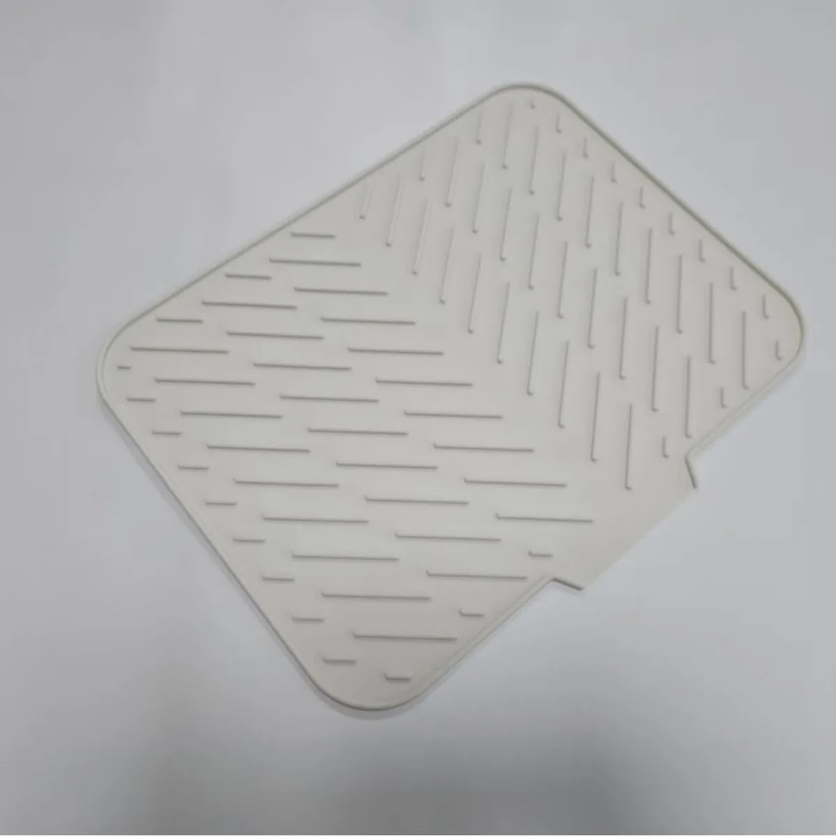 A white silicone drain mat with raised, parallel lines for grip is shown from above.