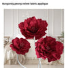A close-up of a deep burgundy velvet fabric applique peony flower in a vase against a white background.