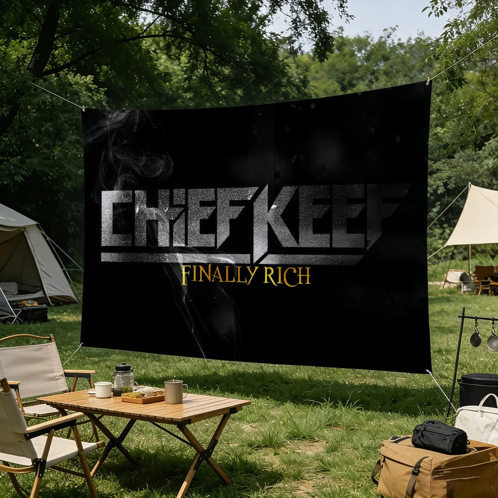 A large black banner with white text reading CHIEFKEEP FINALLY RICH displayed outdoors in a grassy field.