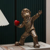 A bronze-colored resin sculpture of a child figure throwing a red heart against a dark green background.