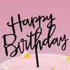 Black acrylic letters spelling happy birthday on a pink cake with yellow accents