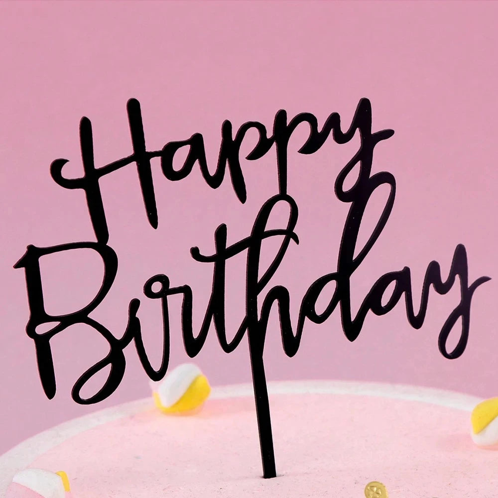 Black acrylic letters spelling happy birthday on a pink cake with yellow accents
