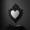 A black ornate wall mirror shaped like a heart with flame detailing mounted on a dark gray wall.