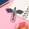 A black metal bookmark shaped like a four-winged dragon is placed on a pink notebook.