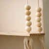 A string of light beige wooden beads hangs from a rustic wooden wall shelf.