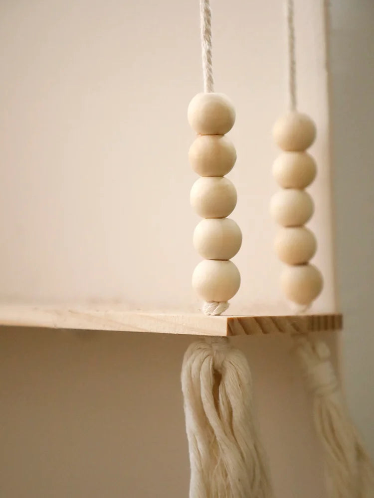 A string of light beige wooden beads hangs from a rustic wooden wall shelf.