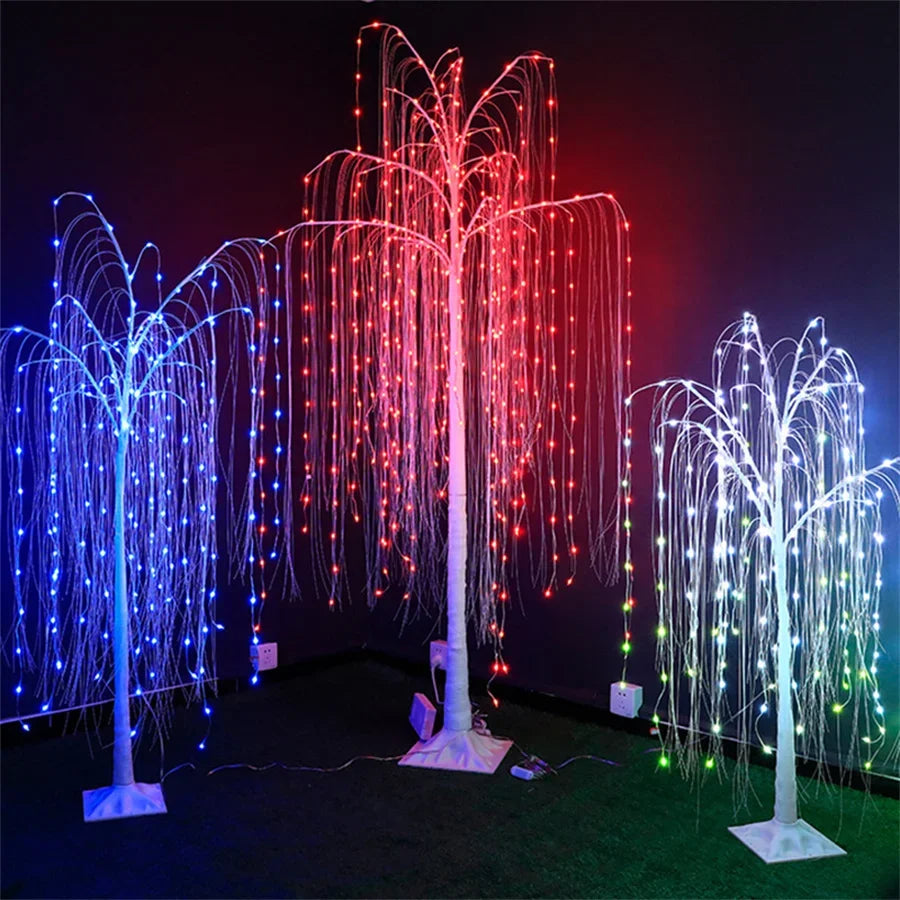 A display of four LED weeping willow trees with multicolored lights illuminating a dark green surface.