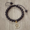 A black beaded bracelet with a gold zodiac charm is displayed on a wooden surface.