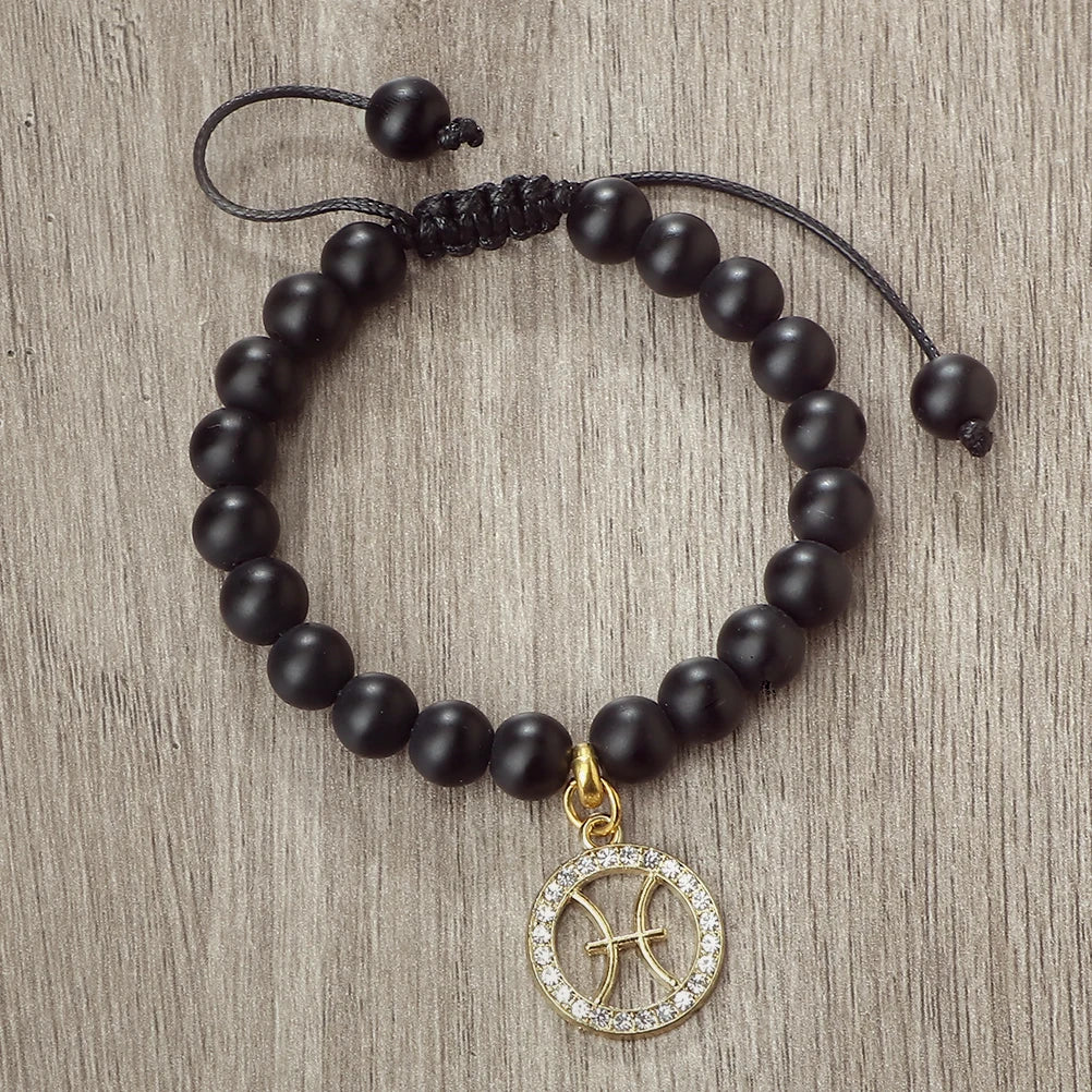 A black beaded bracelet with a gold zodiac charm is displayed on a wooden surface.