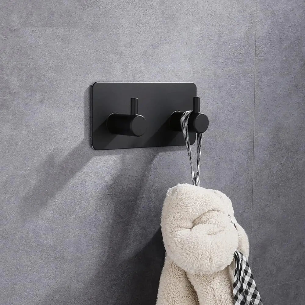 A black self-adhesive wall hook is mounted on a gray wall, with a fluffy white stuffed animal hanging from it.