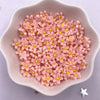 A pile of pink 3D resin flower gems in various shades are displayed in a white dish.