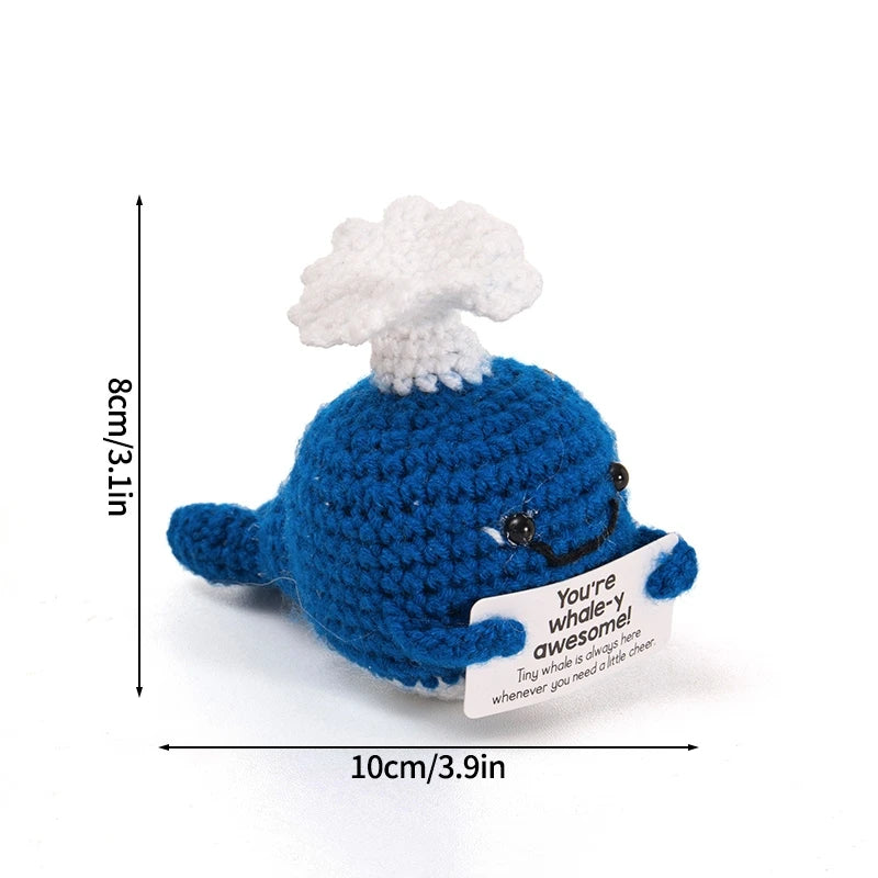 A handmade crochet blue whale doll with a white chef hat and an inspirational slogan tag.