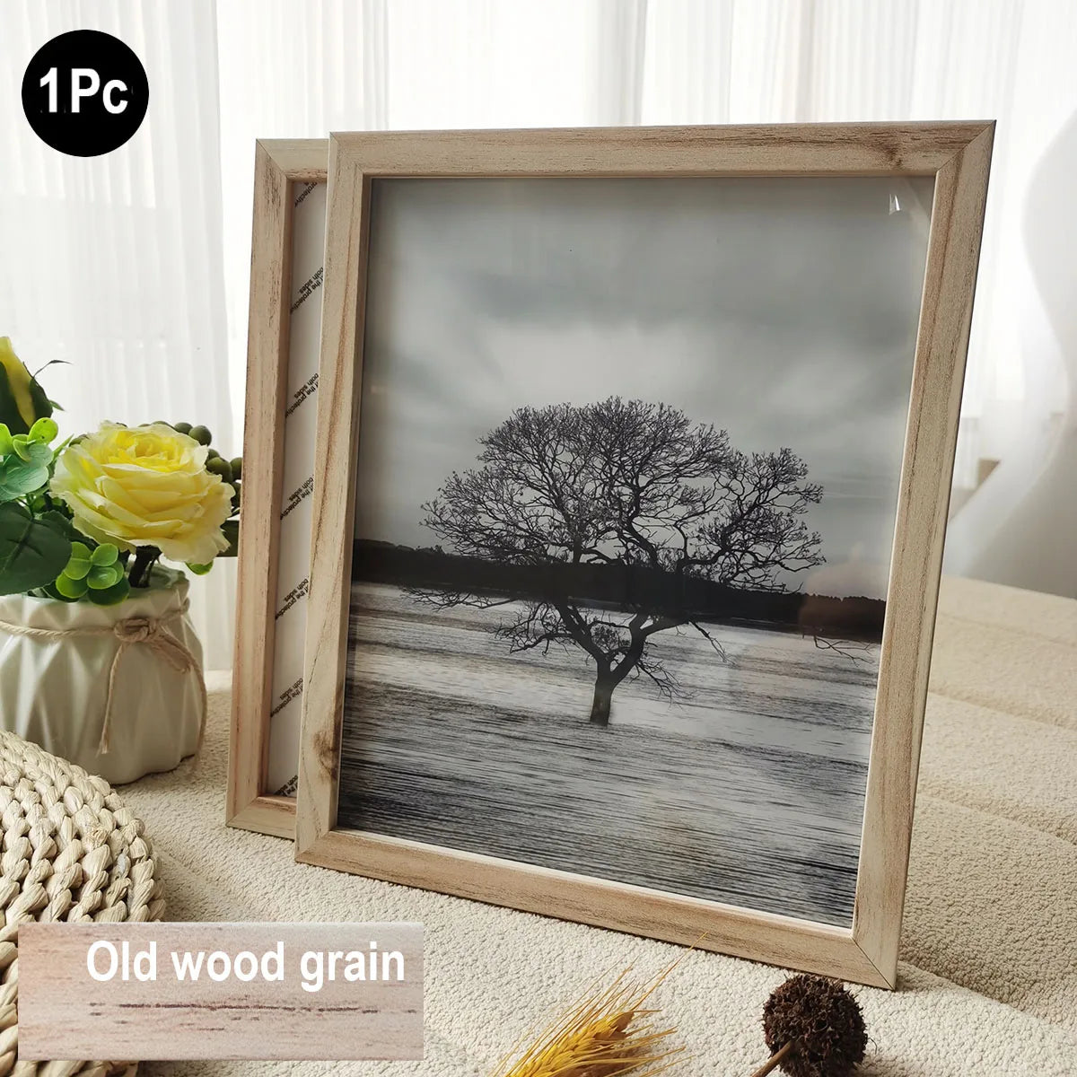 A wooden photo frame displaying a black and white landscape of a tree against a cloudy sky.