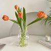 A glass vase holds three vibrant orange tulips with green stems on a white table.