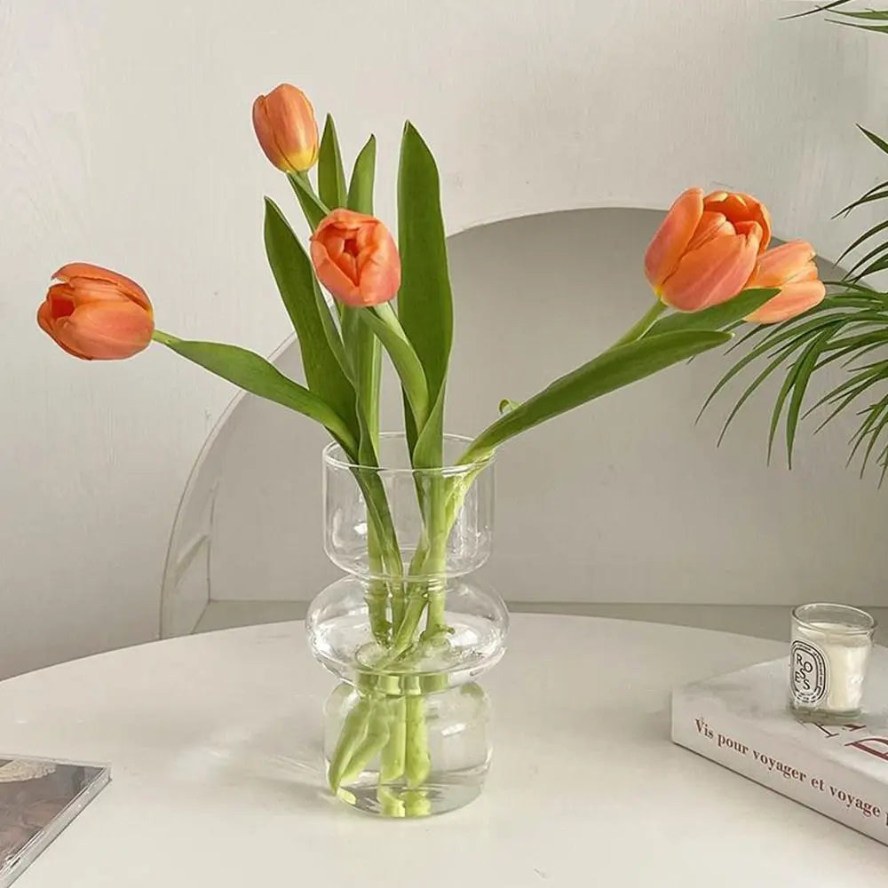 A glass vase holds three vibrant orange tulips with green stems on a white table.