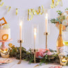 A display of three tall glass hurricane candle holders with gold accents and pink roses on a table.